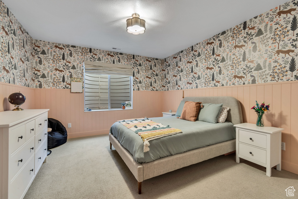 Bedroom with wallpapered walls, a wainscoted wall, and light carpet