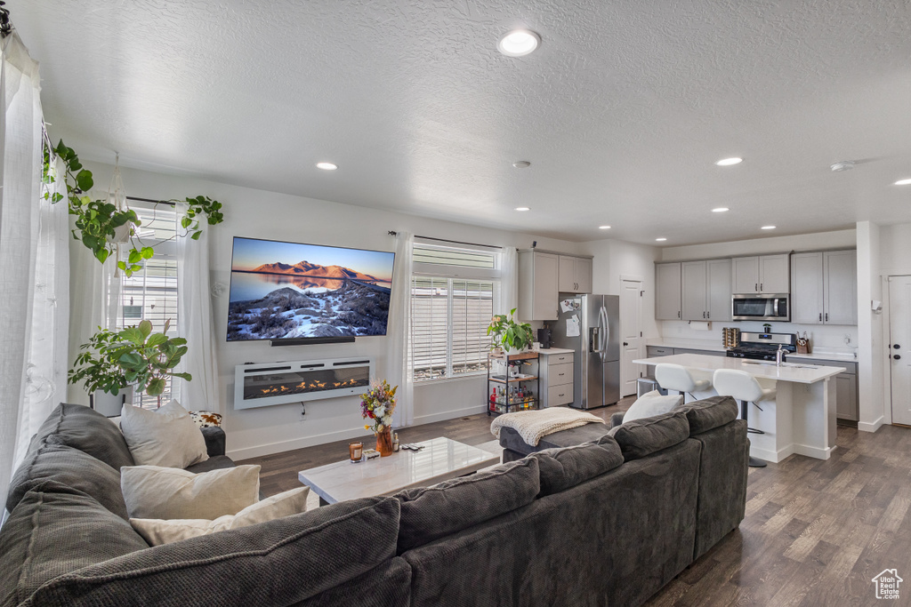 Living room with dark wood-style flooring, recessed lighting, a textured ceiling, and a glass covered fireplace
