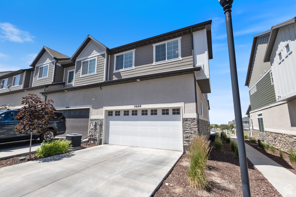Multi unit property with stone siding, an attached garage, driveway, and stucco siding