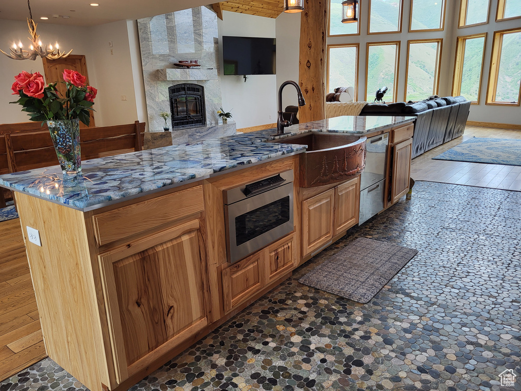 Kitchen featuring open floor plan, appliances with stainless steel finishes, a chandelier, a tile fireplace, and light stone counters