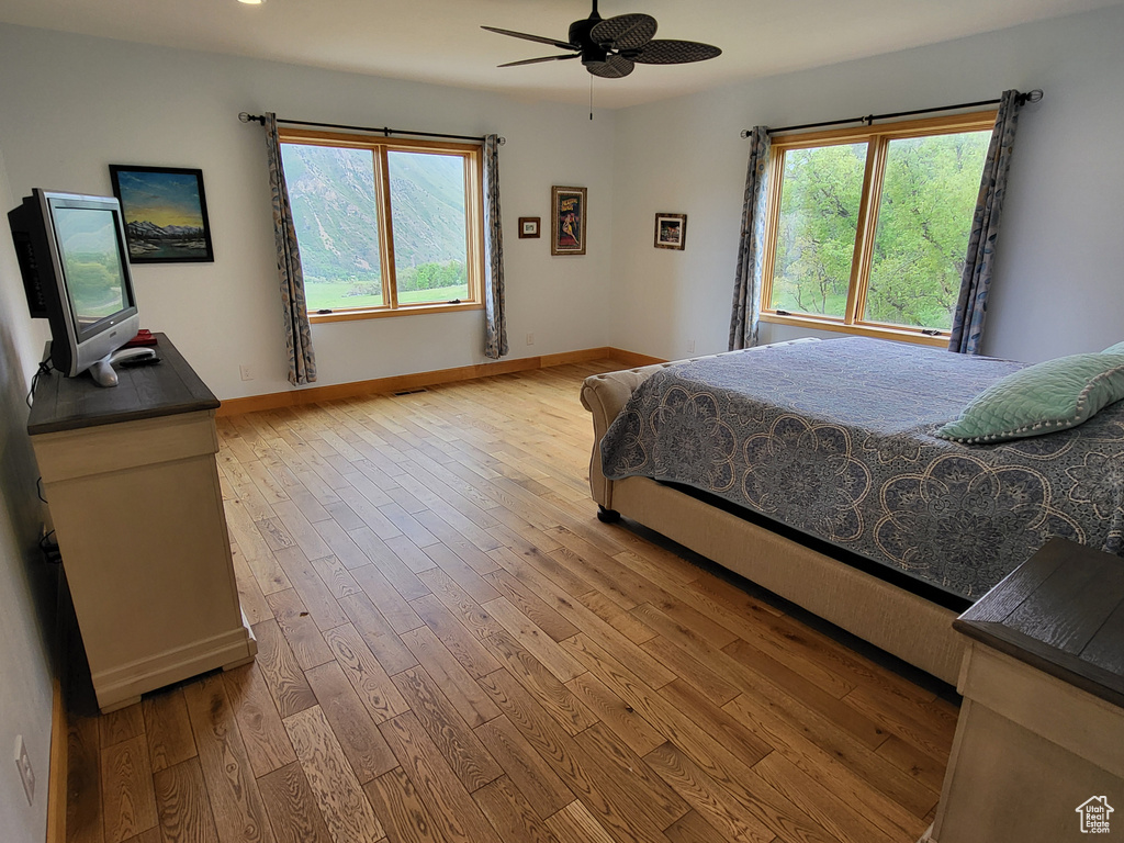 Bedroom with light wood finished floors, multiple windows, and ceiling fan