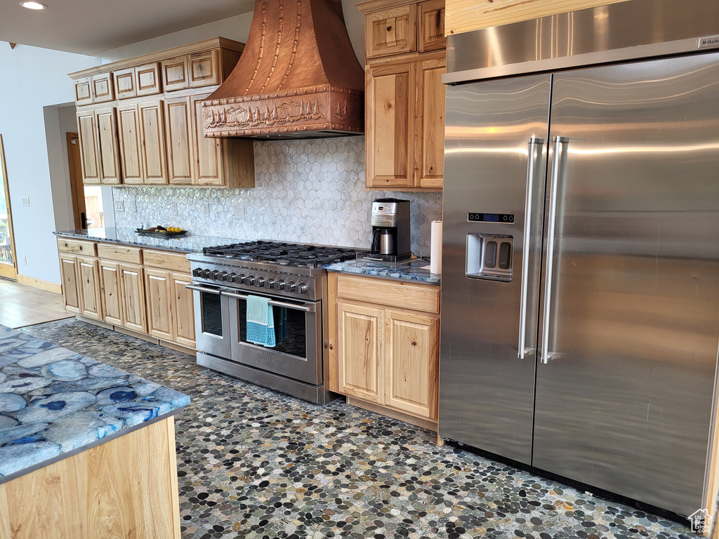 Kitchen with high end appliances, custom exhaust hood, tasteful backsplash, light brown cabinets, and recessed lighting