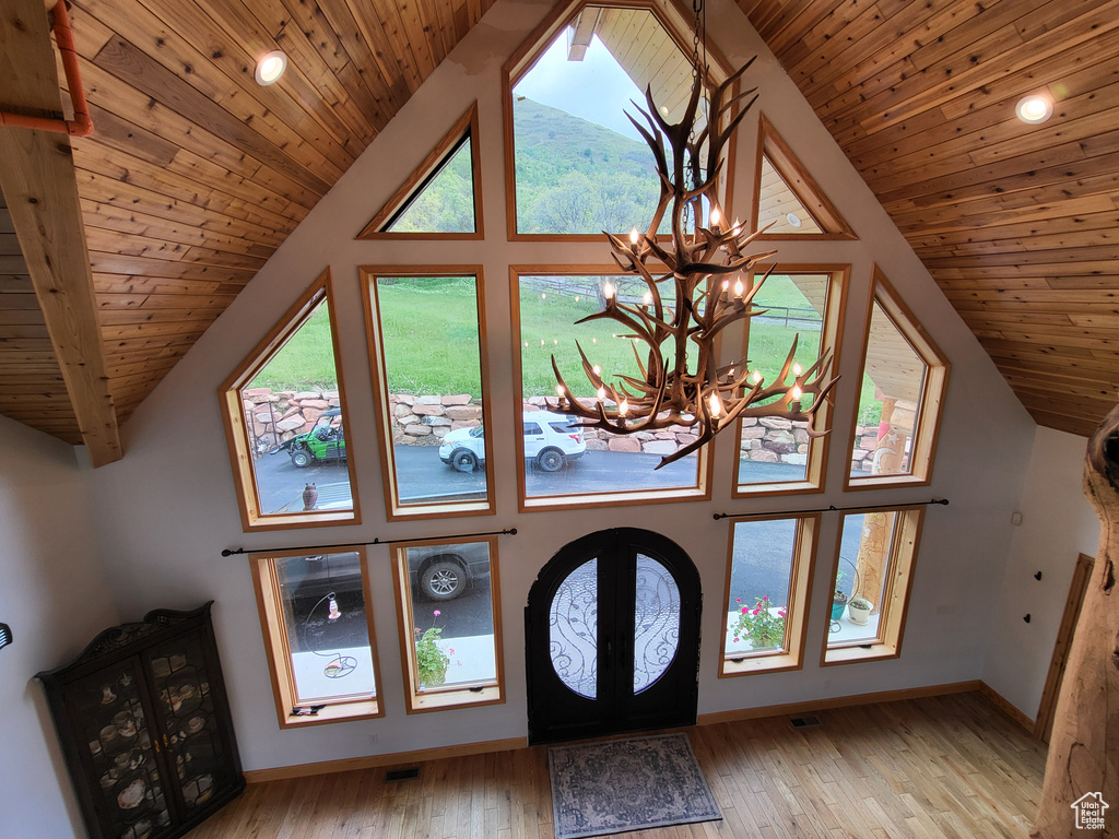 Foyer entrance with a chandelier, vaulted ceiling, wood ceiling, light wood finished floors, and french doors