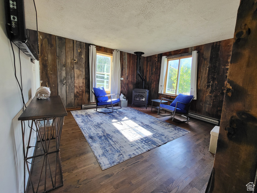 Living area featuring a textured ceiling, a wood stove, dark wood-type flooring, and wooden walls