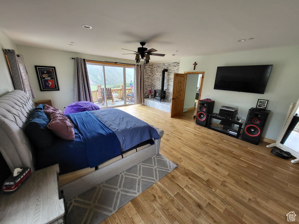 Bedroom featuring a wood stove, light wood finished floors, multiple windows, access to exterior, and recessed lighting