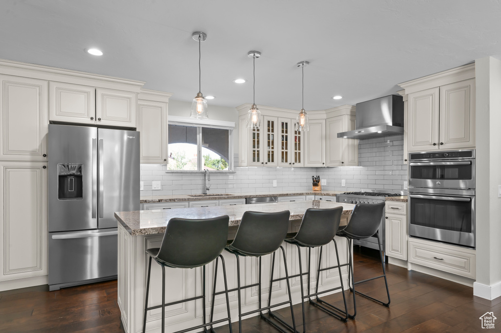 Kitchen featuring appliances with stainless steel finishes, wall chimney range hood, backsplash, light stone countertops, and recessed lighting