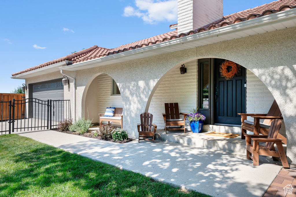 Back of house with a tiled roof, stucco siding, a chimney, a garage, and covered porch
