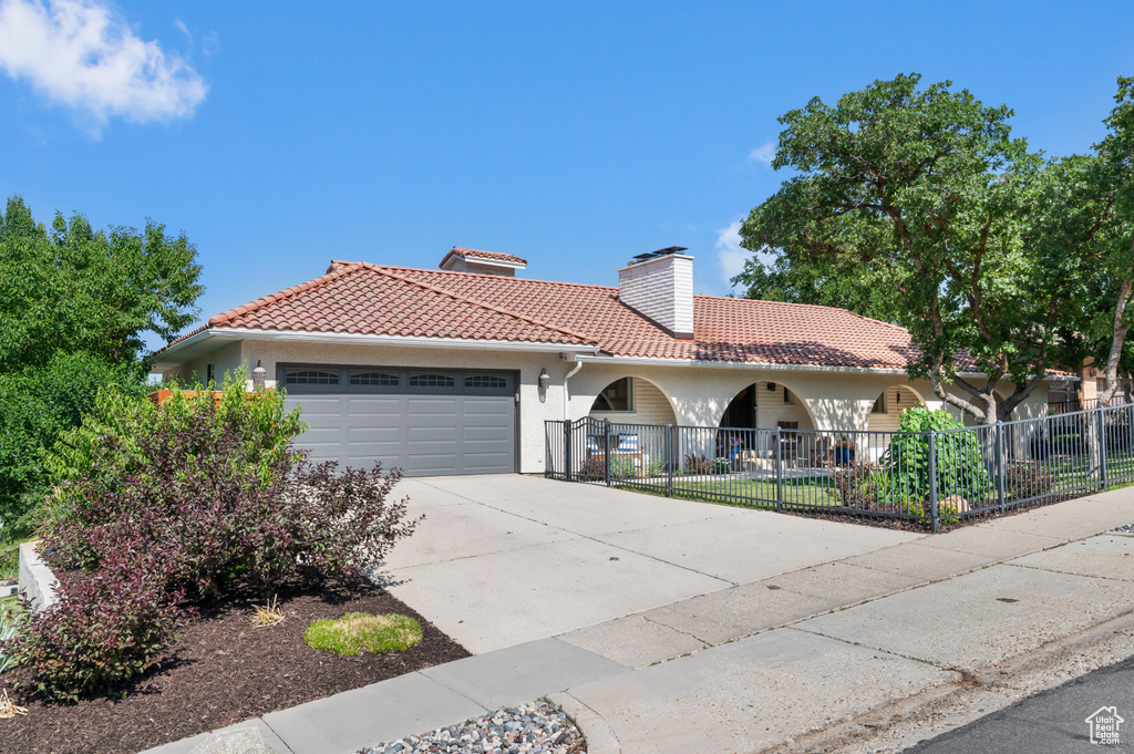 Mediterranean / spanish home with an attached garage, a tiled roof, a chimney, driveway, and stucco siding