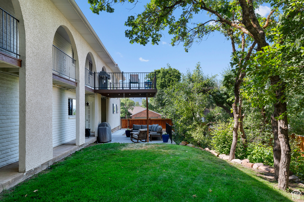 View of grassy yard featuring an outdoor hangout area, a balcony, and a patio area