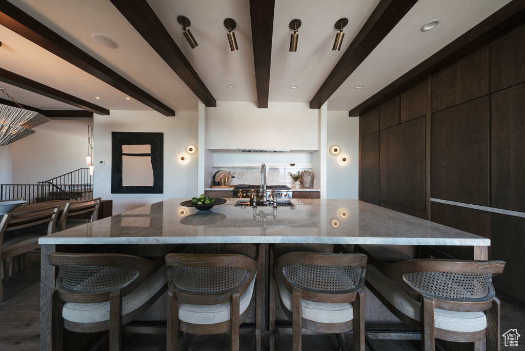 Kitchen with modern cabinets, beamed ceiling, a breakfast bar area, light stone countertops, and dark brown cabinetry
