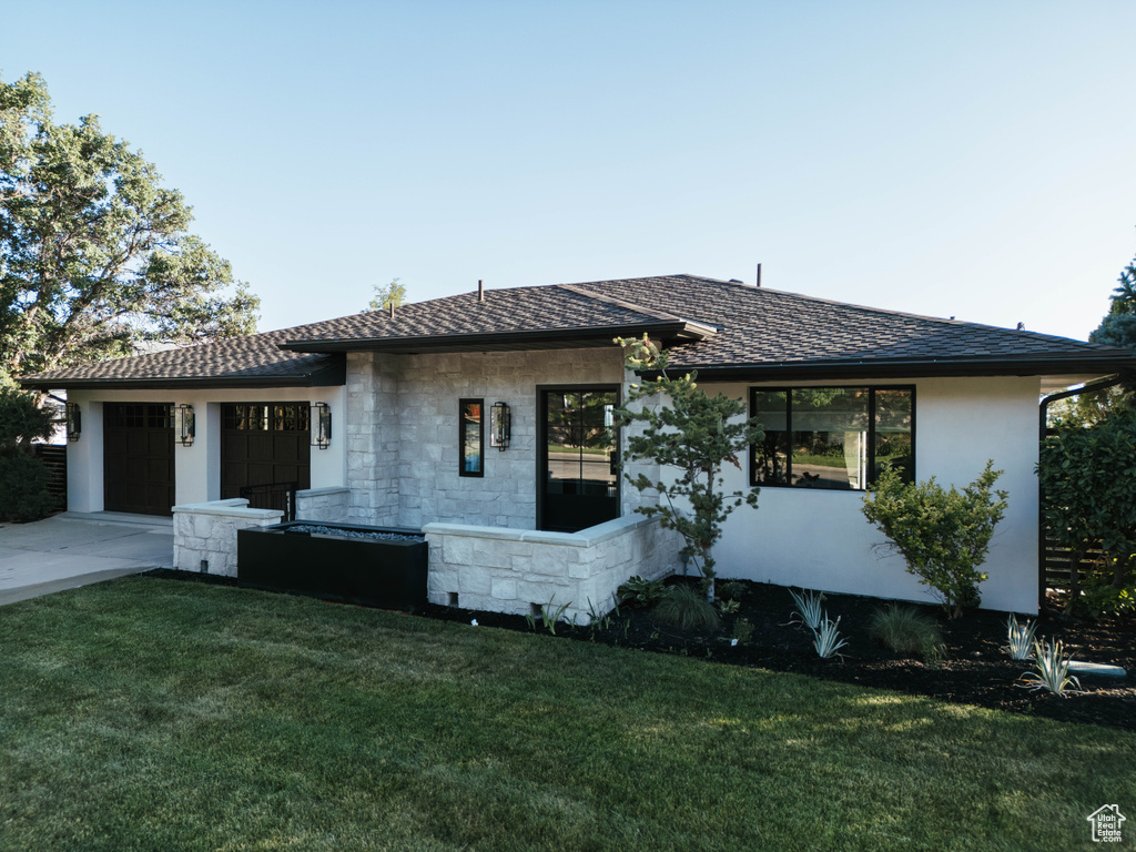 View of front of home featuring a front lawn, an attached garage, concrete driveway, stone siding, and stucco siding