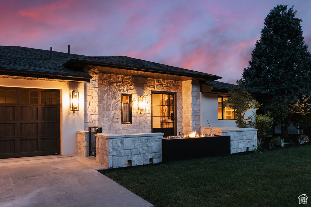 View of front facade with stone siding, a garage, a front yard, a shingled roof, and driveway