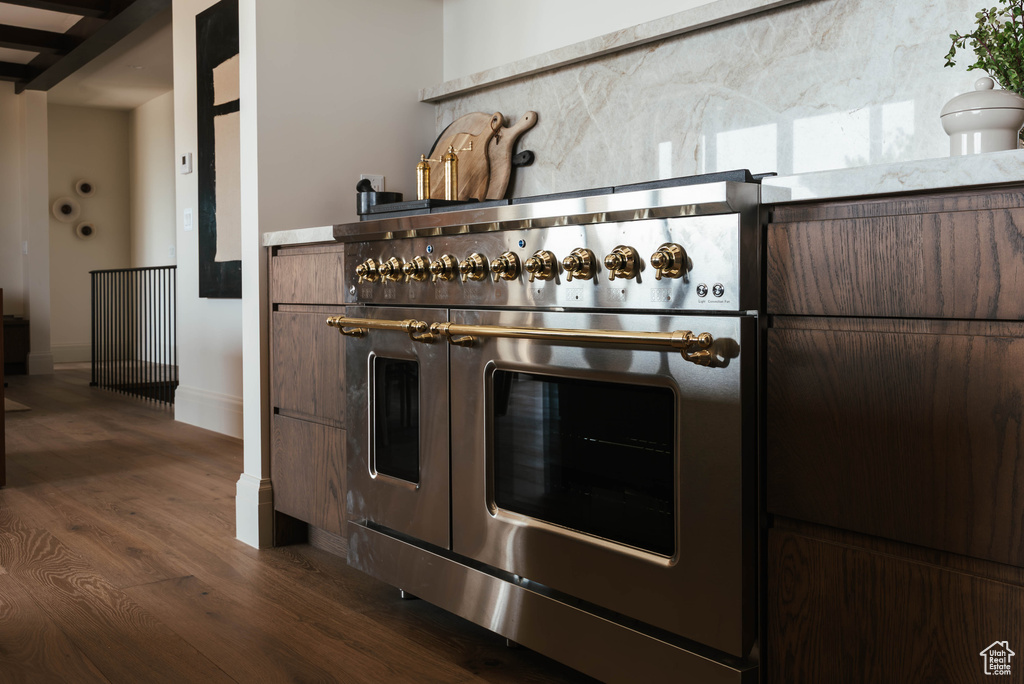 Kitchen view of range with two ovens, dark wood-style flooring, dark brown cabinetry, and tasteful backsplash