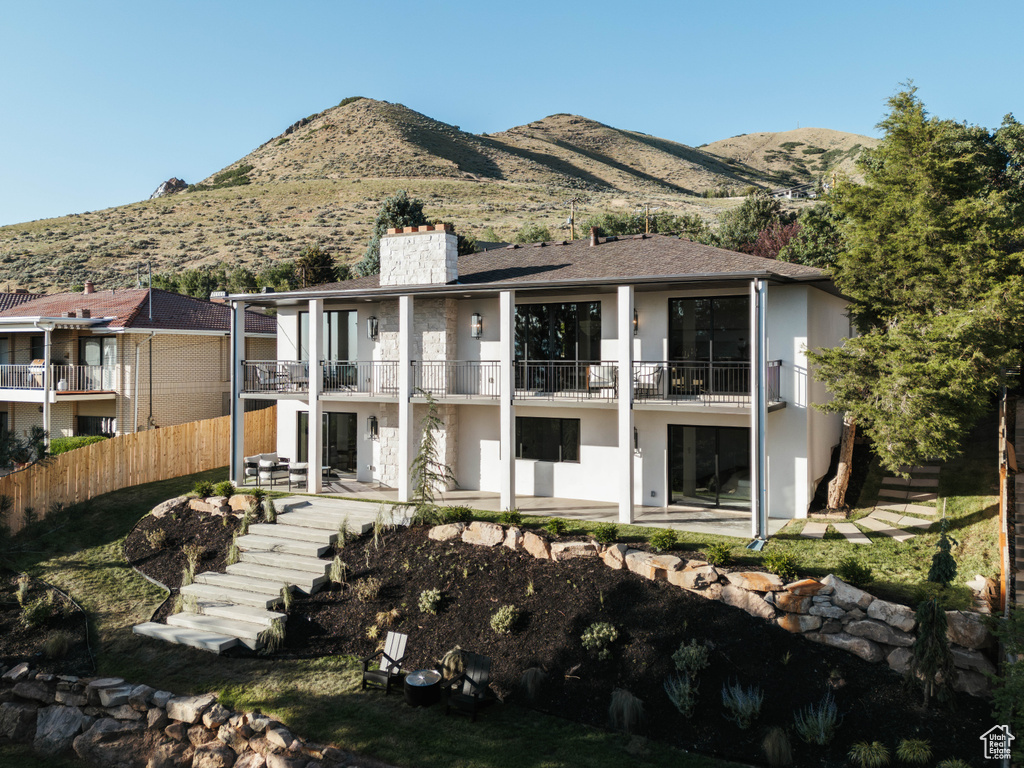 Back of property featuring a balcony, a chimney, stucco siding, and a patio