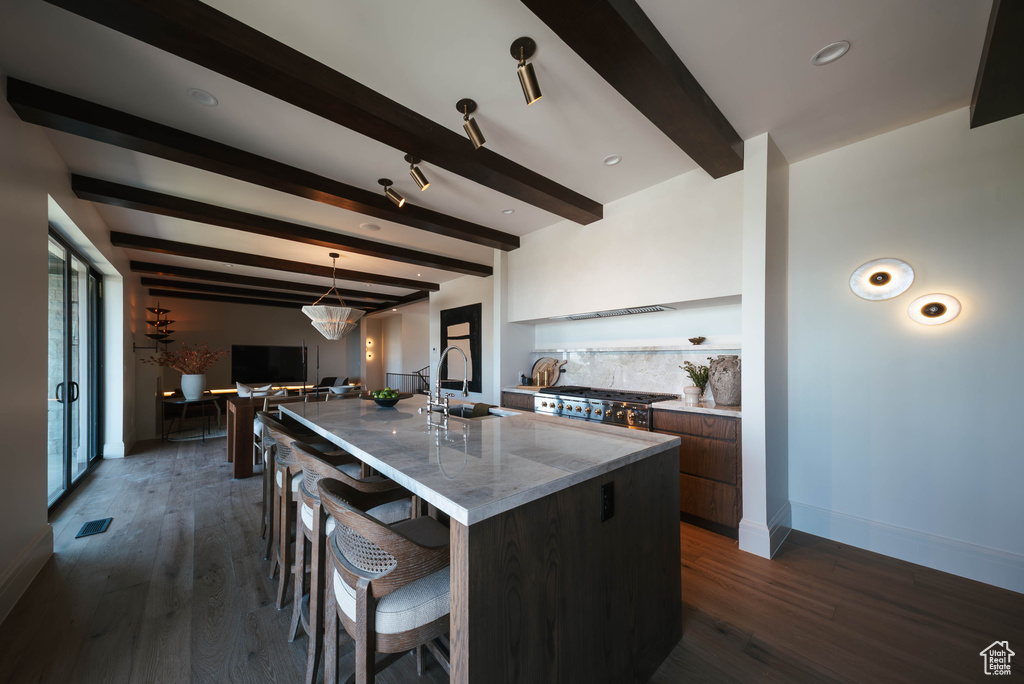 Kitchen featuring modern cabinets, beam ceiling, a large island with sink, a kitchen bar, and dark wood-style floors