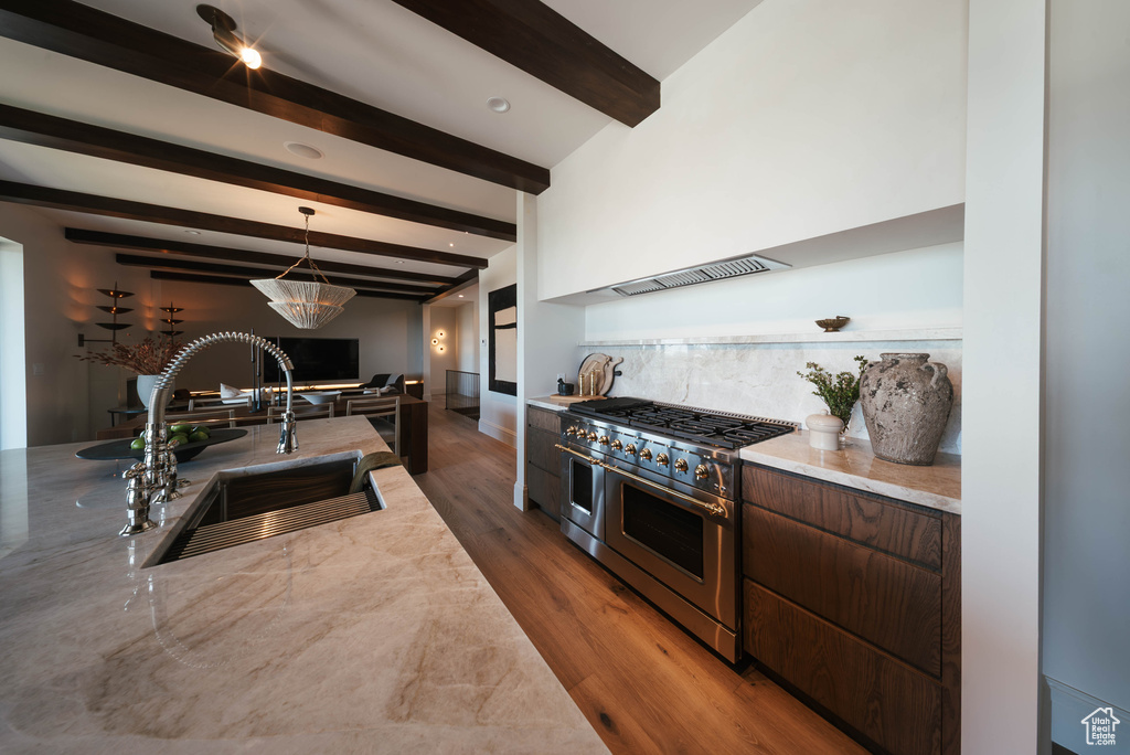 Kitchen with range with two ovens, beam ceiling, wood finished floors, custom range hood, and hanging light fixtures