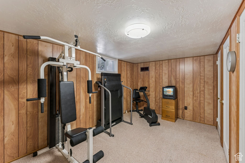 Workout area with wooden walls, a textured ceiling, and light carpet