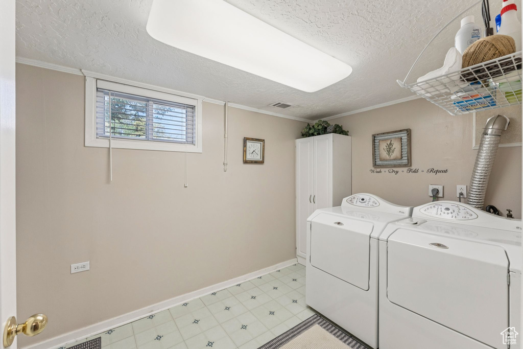 Laundry room featuring cabinet space, a textured ceiling, independent washer and dryer, and ornamental molding