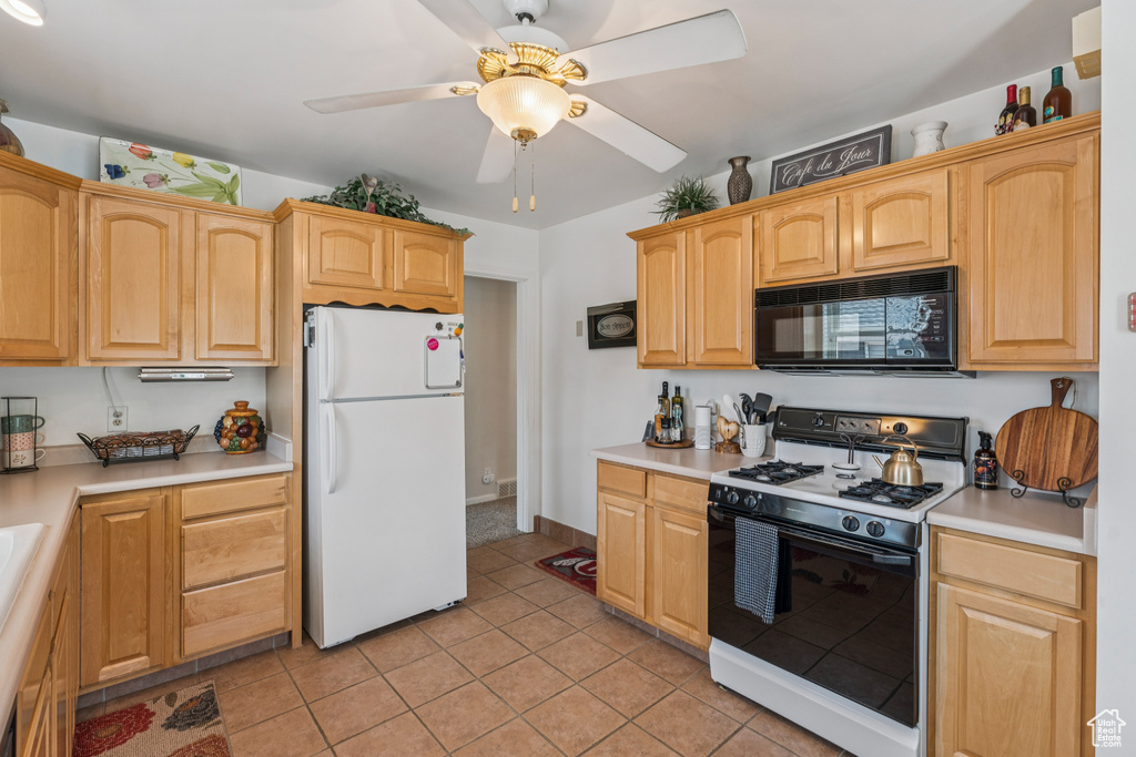 Kitchen with freestanding refrigerator, gas range, black microwave, a ceiling fan, and light tile patterned floors