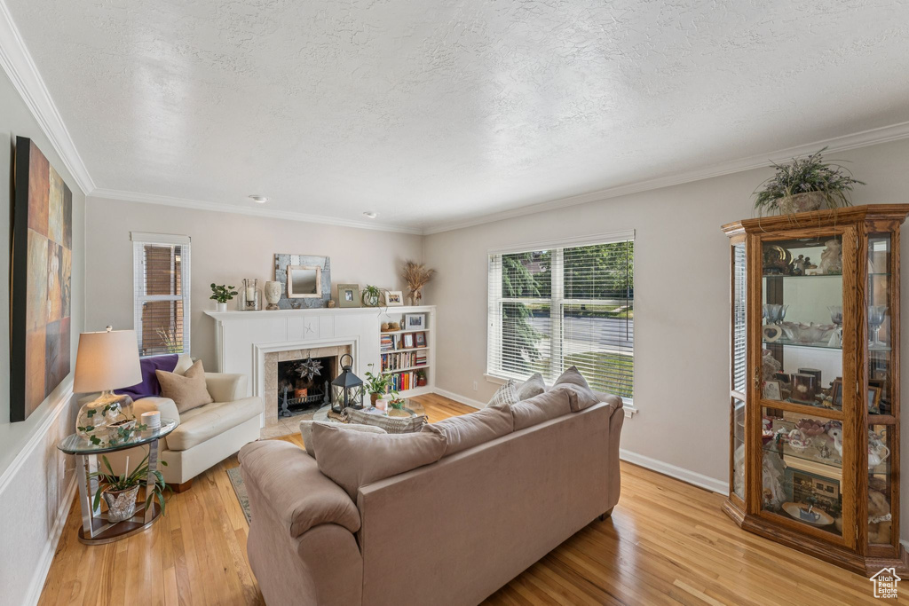 Living area with light wood finished floors, a tiled fireplace, a textured ceiling, and crown molding