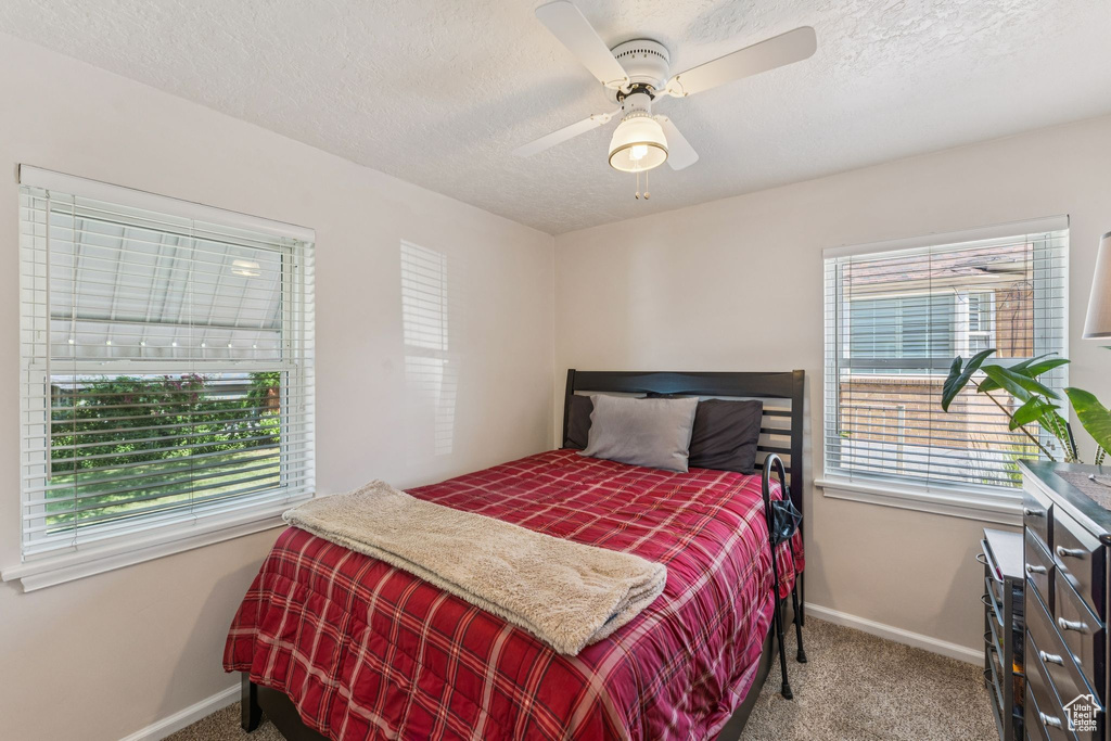 Carpeted bedroom featuring multiple windows, a textured ceiling, and ceiling fan