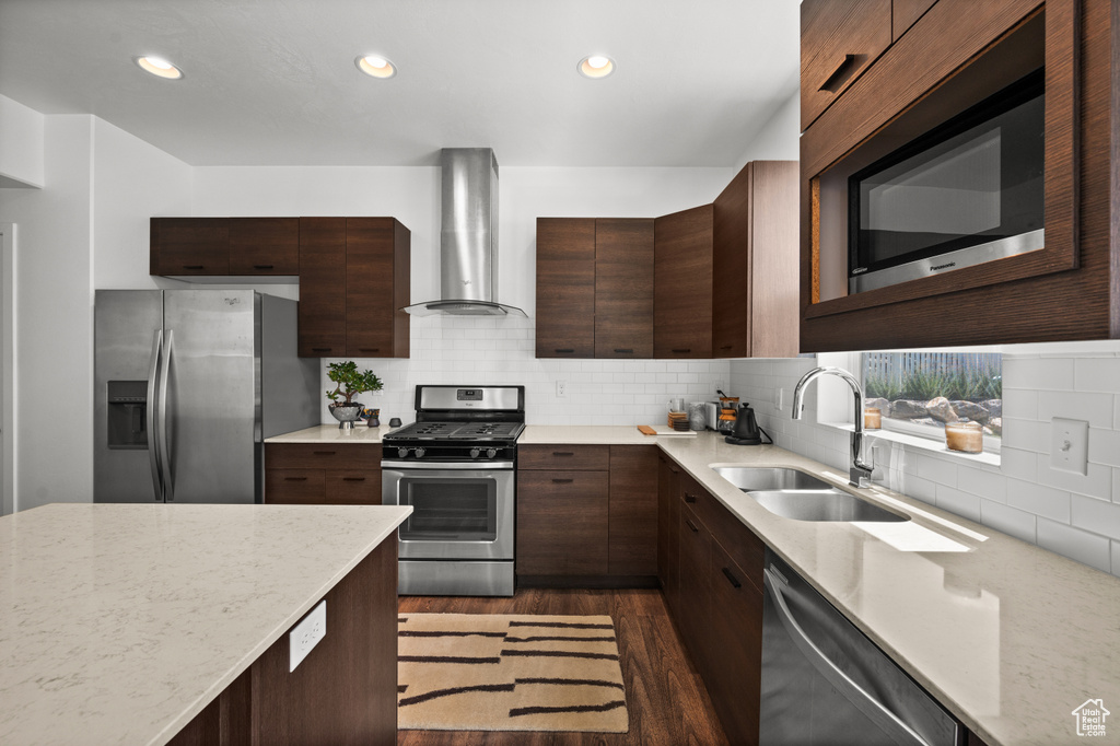Kitchen with stainless steel appliances, wall chimney range hood, dark wood-style floors, decorative backsplash, and light stone counters