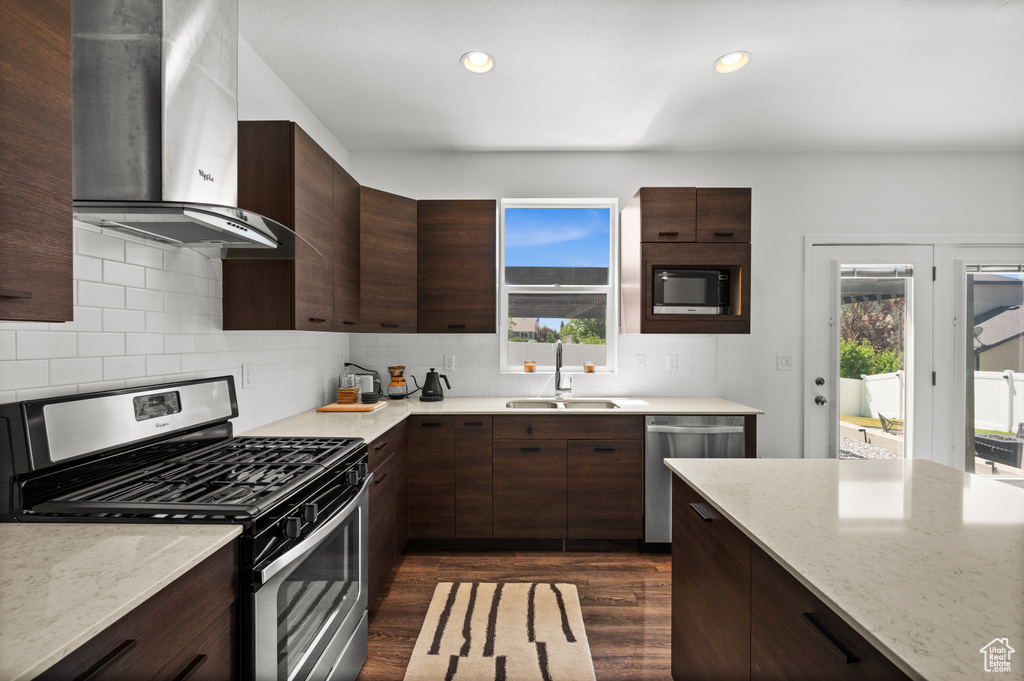 Kitchen featuring appliances with stainless steel finishes, range hood, plenty of natural light, dark wood finished floors, and recessed lighting