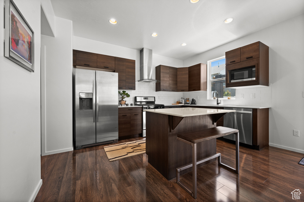 Kitchen with appliances with stainless steel finishes, wall chimney exhaust hood, modern cabinets, a breakfast bar area, and decorative backsplash