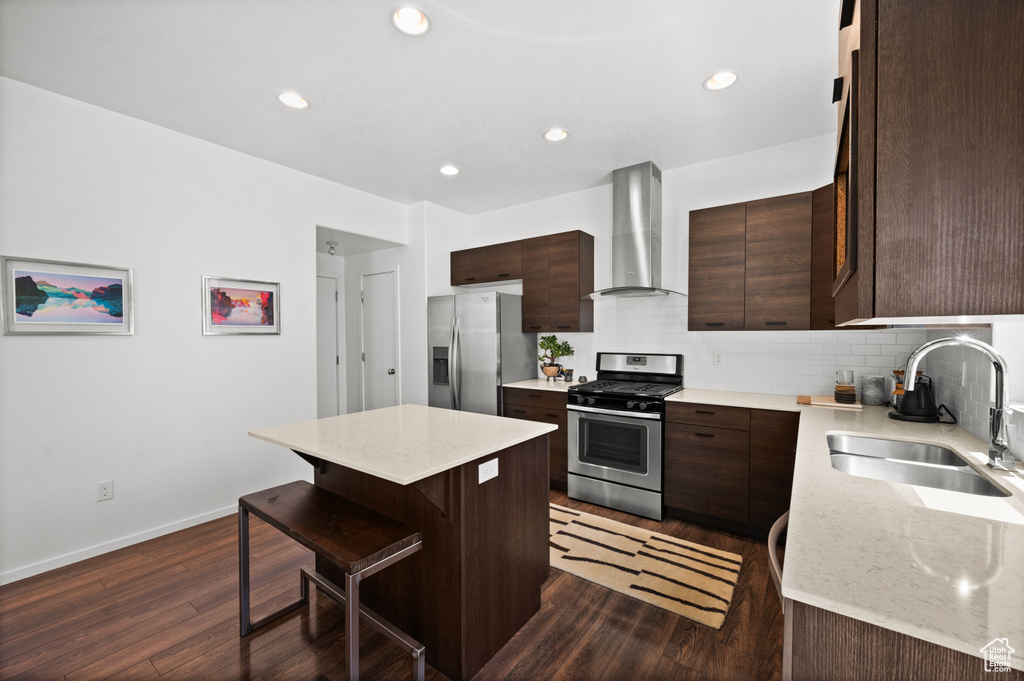 Kitchen featuring stainless steel appliances, wall chimney exhaust hood, a center island, a breakfast bar, and dark brown cabinets