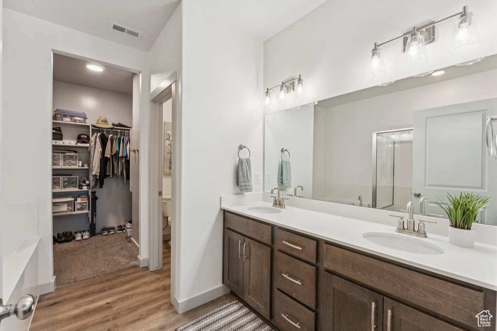 Bathroom with double vanity, wood finished floors, a spacious closet, and a stall shower