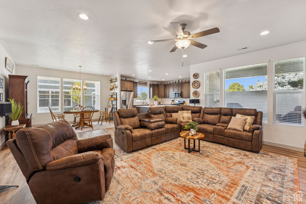 Living area with ceiling fan, light wood finished floors, recessed lighting, and a chandelier
