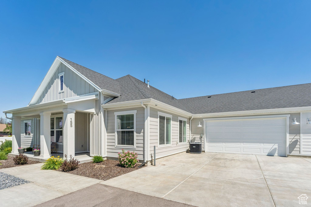 View of front of house featuring concrete driveway, a garage, covered porch, roof with shingles, and board and batten siding