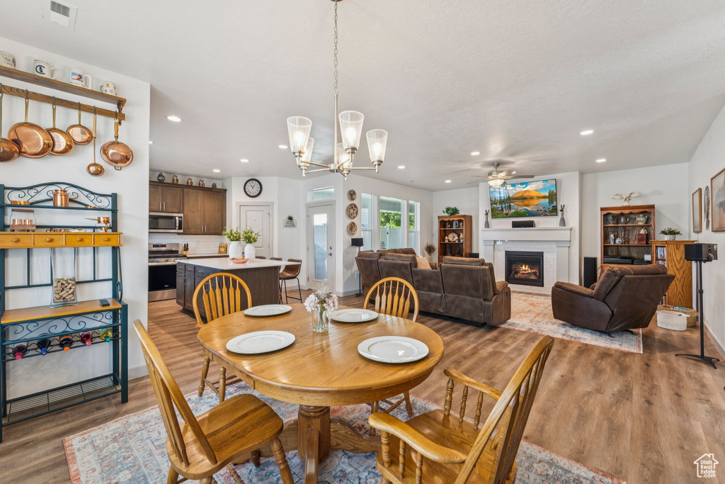 Dining space with ceiling fan, light wood-style floors, a chandelier, a warm lit fireplace, and recessed lighting