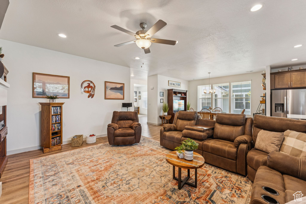 Living room featuring light wood-type flooring, a ceiling fan, recessed lighting, and a chandelier