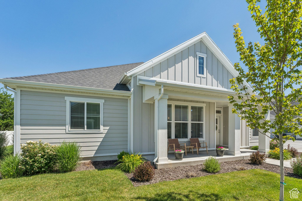 Rear view of house featuring board and batten siding, a porch, a shingled roof, and a yard