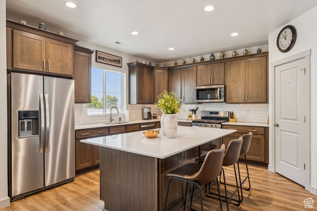Kitchen with appliances with stainless steel finishes, a center island, light wood finished floors, a kitchen breakfast bar, and recessed lighting