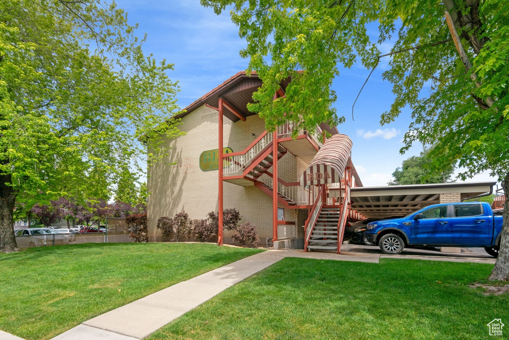 View of front facade with stairs, a front yard, a carport, and brick siding