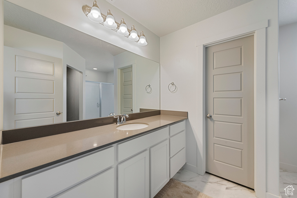 Bathroom featuring marble look tiles, vanity, and a shower with door