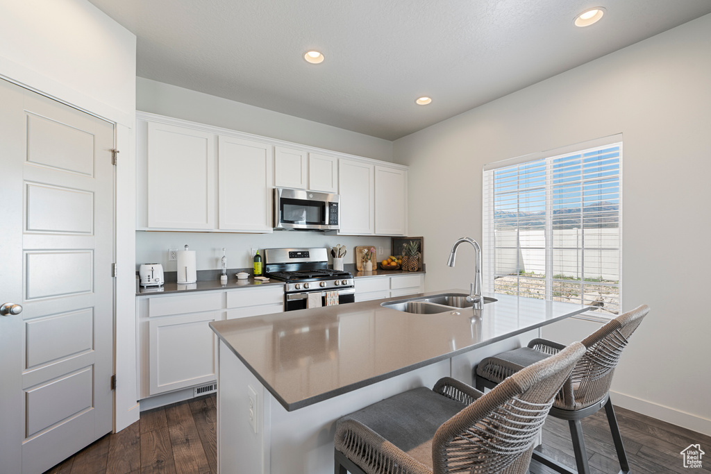 Kitchen featuring stainless steel appliances, a breakfast bar area, a center island with sink, recessed lighting, and white cabinetry