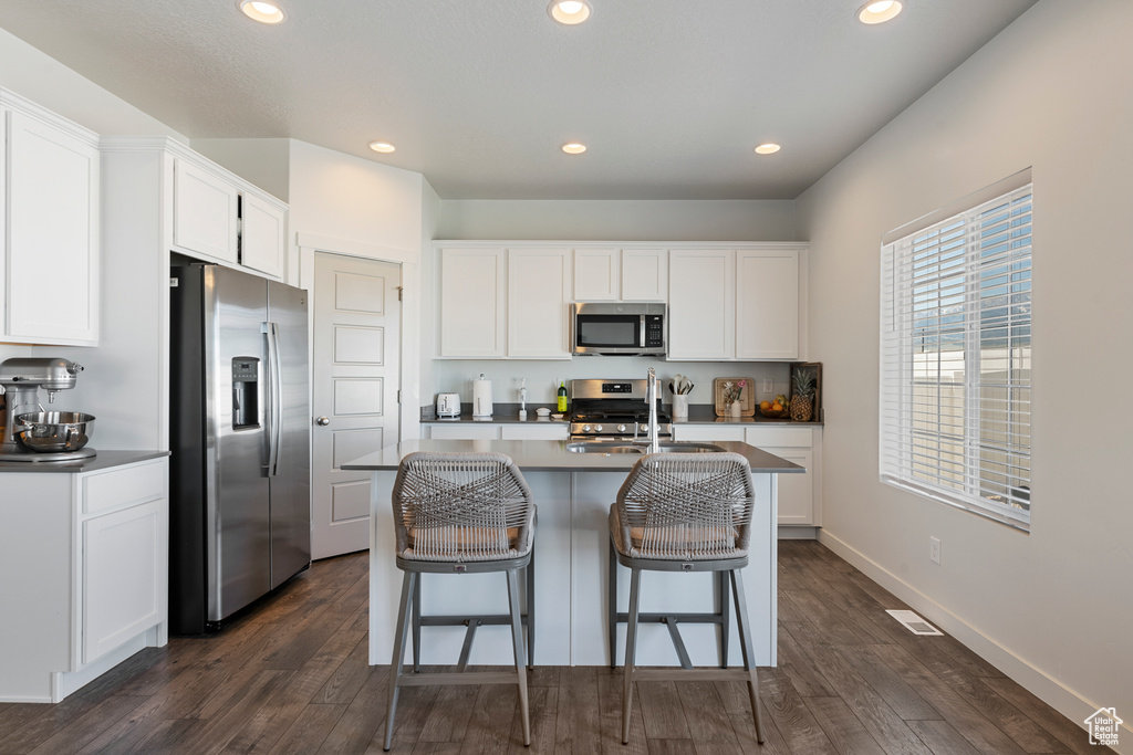 Kitchen with stainless steel appliances, recessed lighting, dark wood finished floors, white cabinets, and a kitchen bar