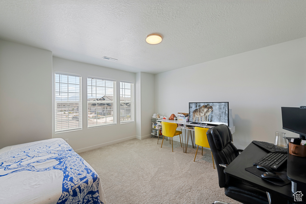 Carpeted bedroom featuring an office area and a textured ceiling