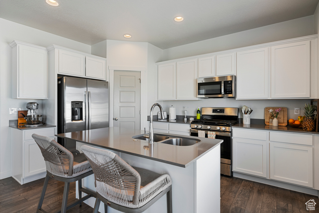 Kitchen with stainless steel appliances, dark countertops, recessed lighting, a breakfast bar, and an island with sink