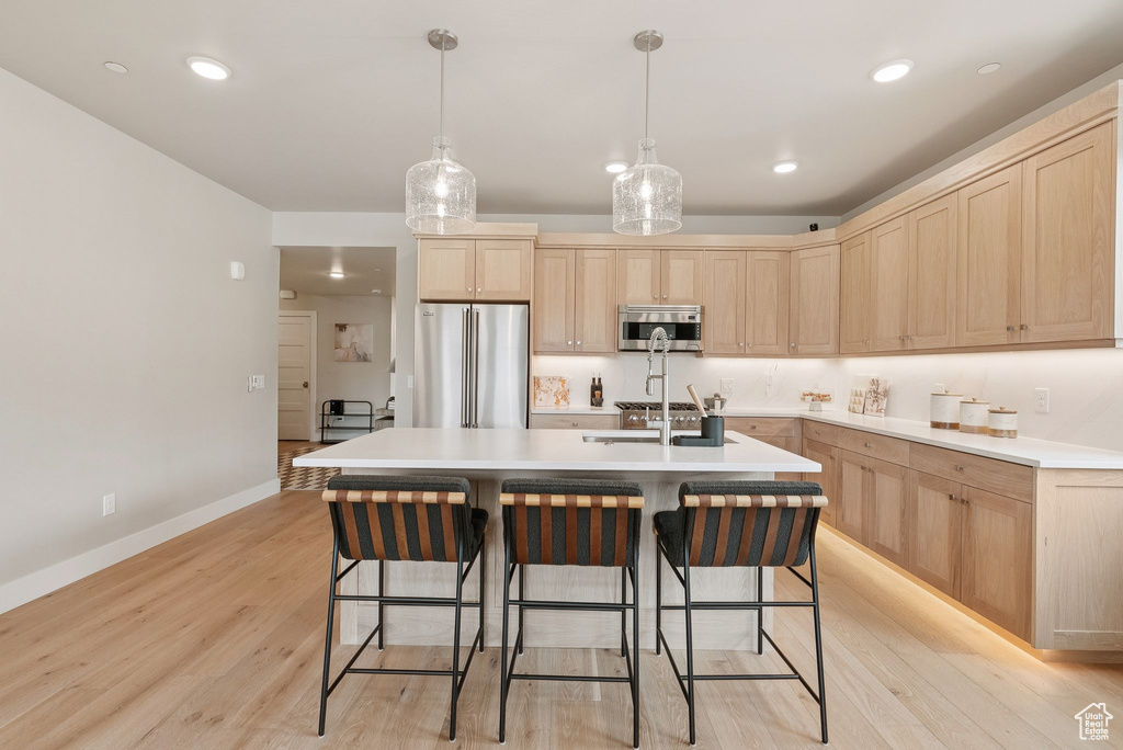 Kitchen featuring light brown cabinets, freestanding refrigerator, light wood finished floors, light countertops, and a breakfast bar