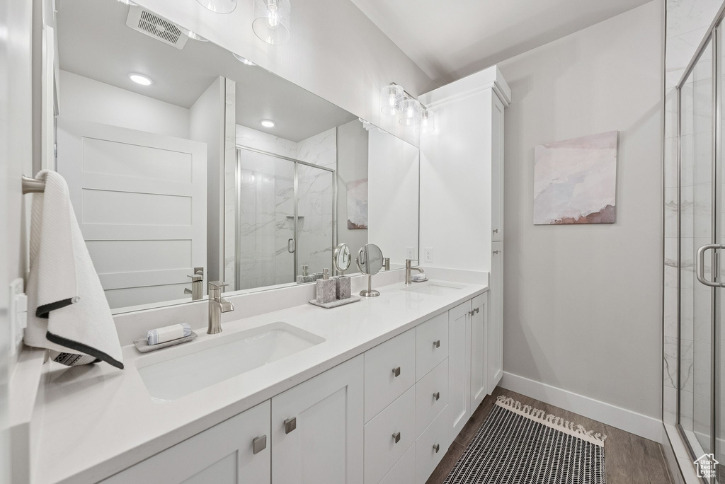 Full bath with double vanity, a shower stall, and wood finished floors