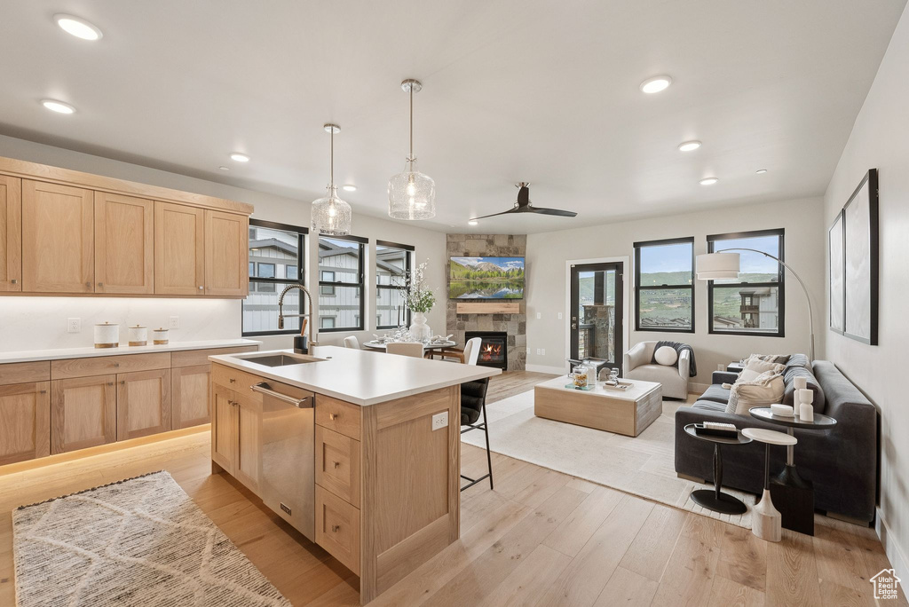 Kitchen with light brown cabinetry, stainless steel dishwasher, a fireplace, light wood finished floors, and light countertops