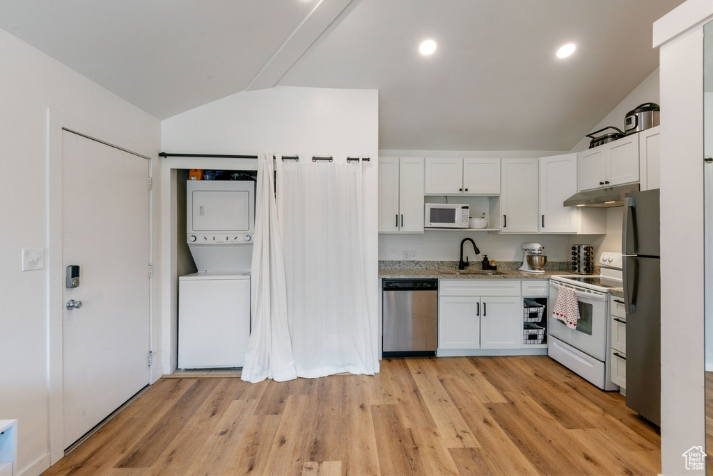Kitchen with stainless steel appliances, stacked washer / drying machine, vaulted ceiling, white cabinetry, and under cabinet range hood