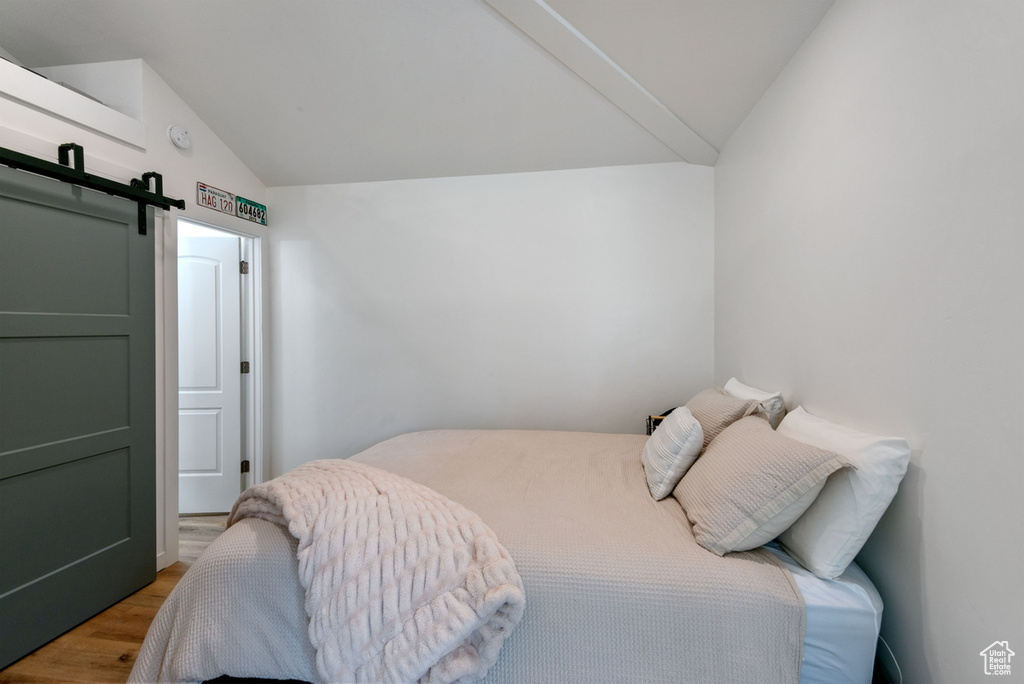 Bedroom with vaulted ceiling, wood finished floors, and a barn door
