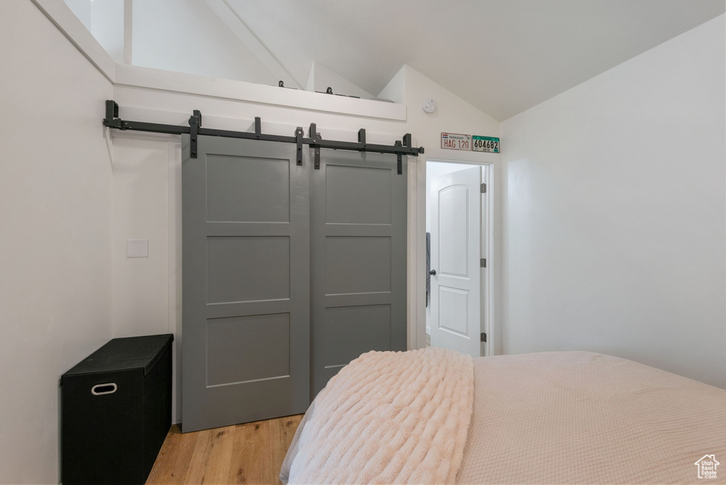 Bedroom with vaulted ceiling, light wood-type flooring, a barn door, and a closet