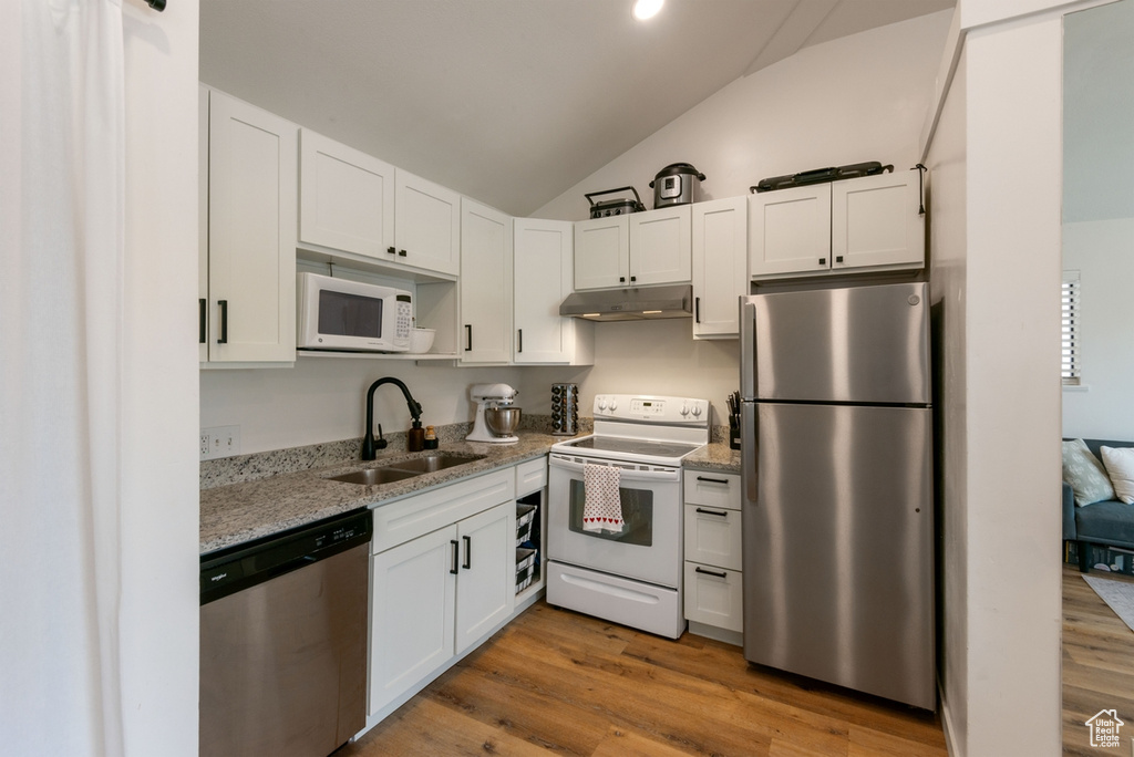 Kitchen featuring appliances with stainless steel finishes, under cabinet range hood, vaulted ceiling, white cabinetry, and light stone countertops