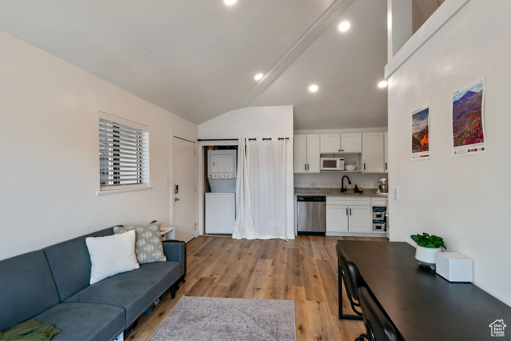 Living area with stacked washer and clothes dryer, light wood finished floors, and high vaulted ceiling